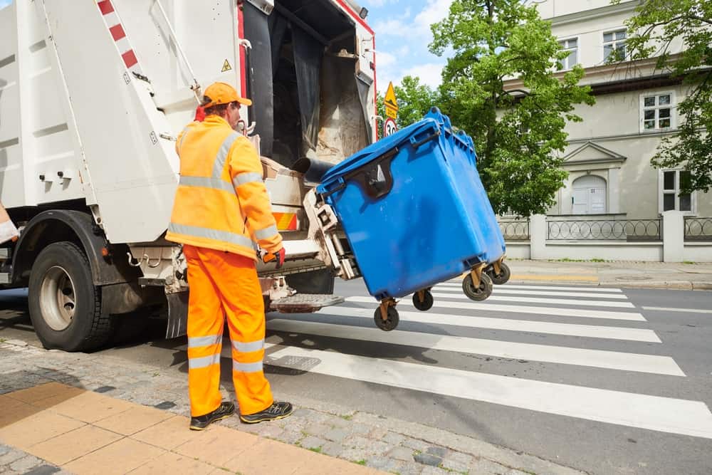 garbage and waste removal services. Worker loading waste bin into truck at city