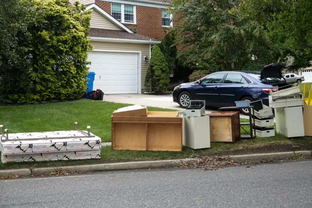 Assorted furniture and mattresses are placed on the curb outside a suburban CA house, near a parked car with its trunk open, likely set out for disposal or donation with Junk Removal San Francisco County.